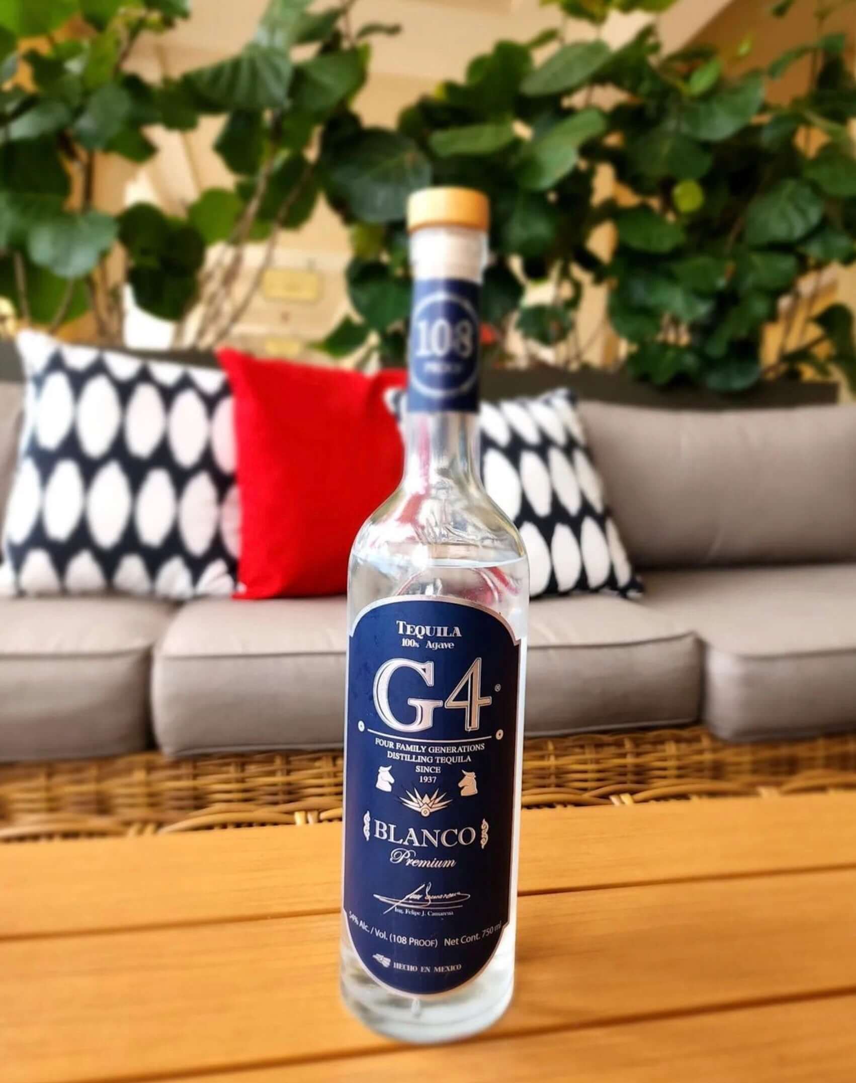G4 Blanco Tequila bottle displayed on a sofa with greenery in the background, showcasing its elegant design.