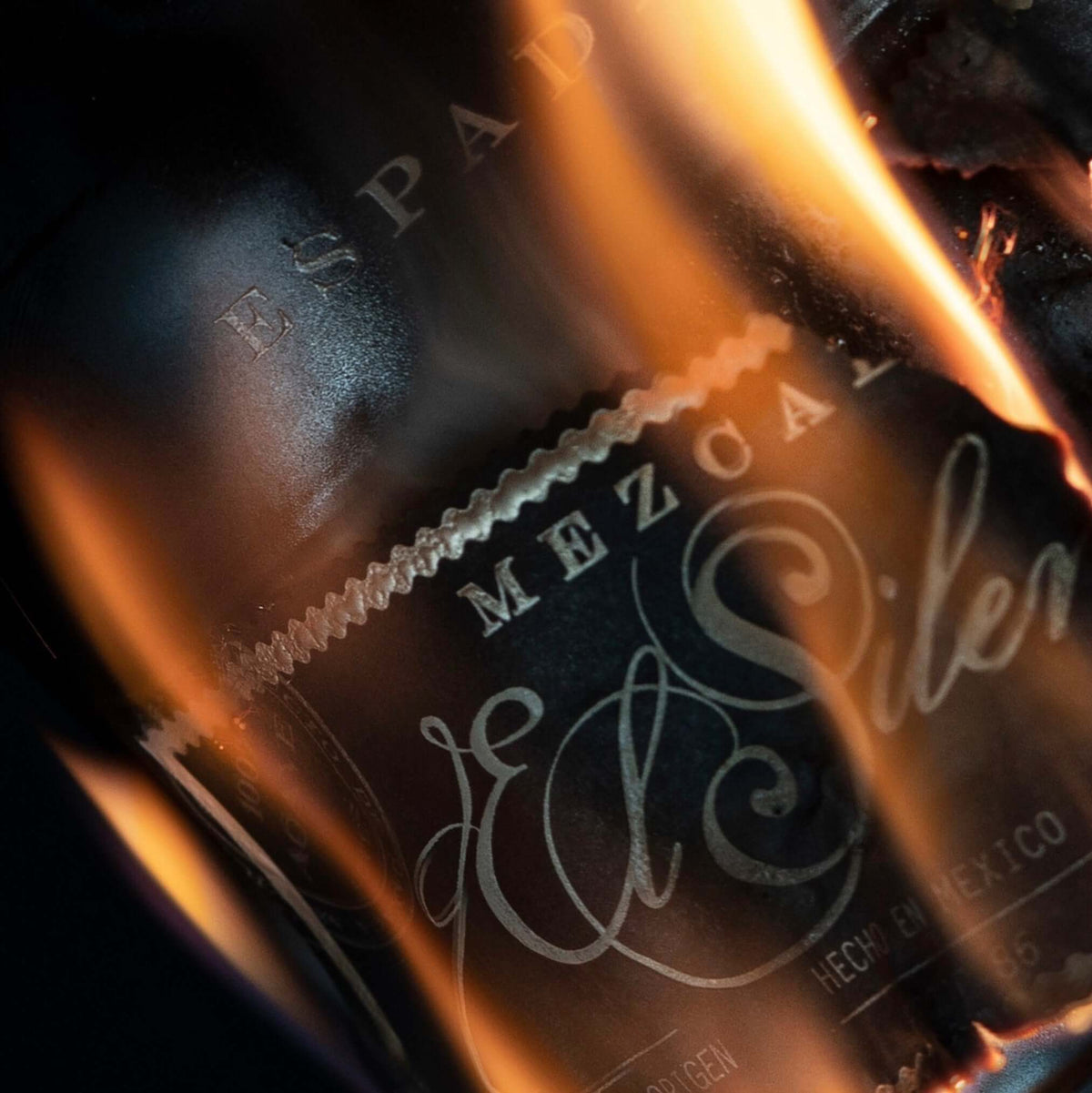 El Silencio Espadín Mezcal bottle with fire background showcasing its sleek design and robust flavor.