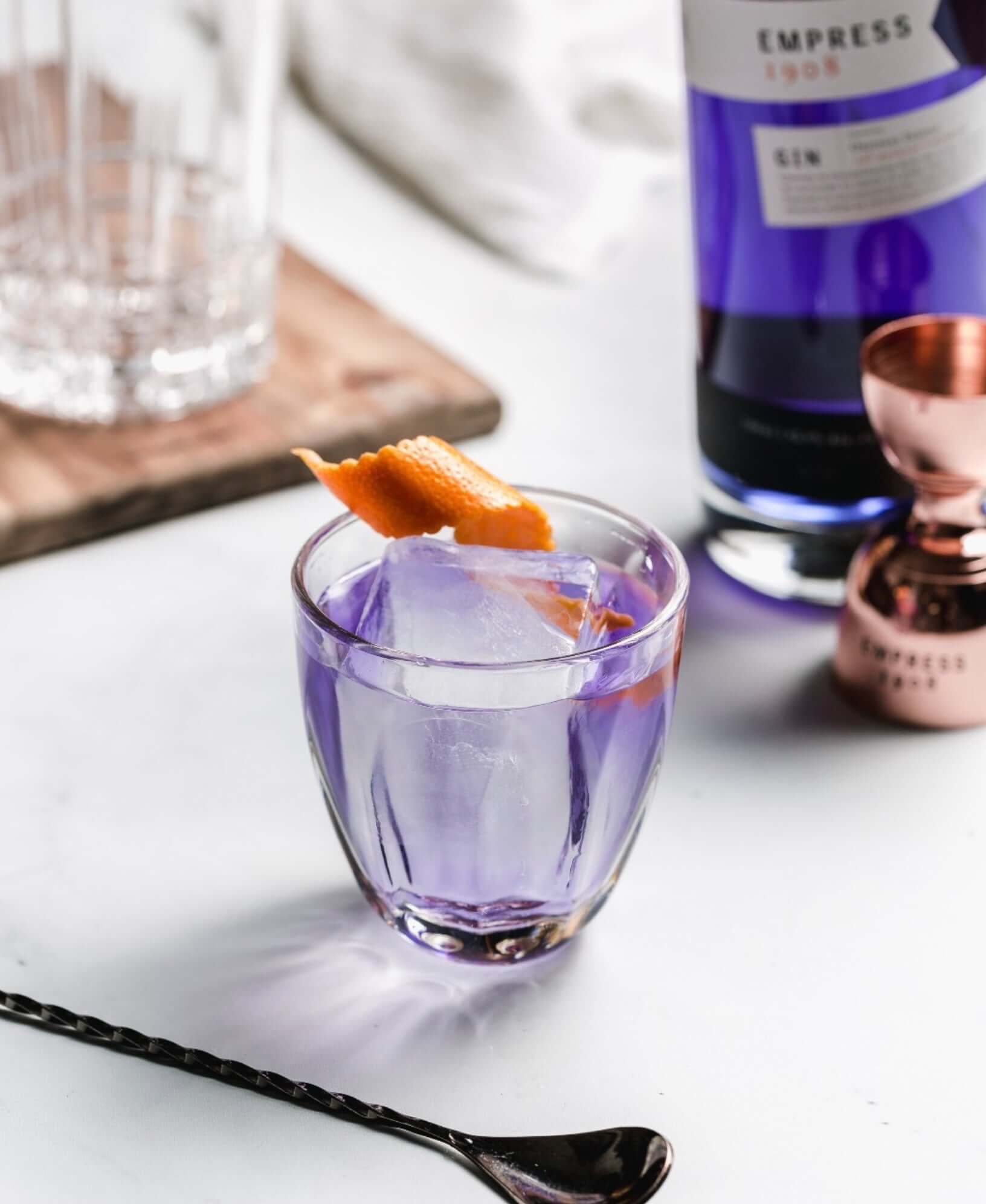 Glass of Empress 1908 Gin cocktail with ice and an orange twist, showcasing its vibrant color and craftsmanship.