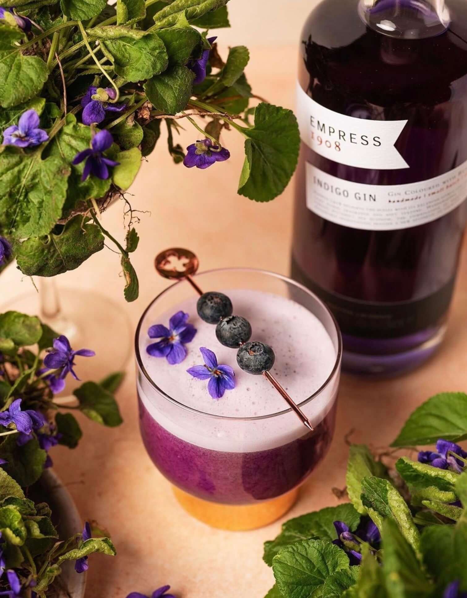 Empress 1908 Gin cocktail garnished with blueberries and edible flowers, showcasing vibrant colors and botanical ingredients.