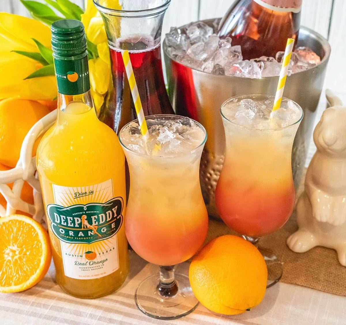 Deep Eddy Orange Vodka bottle beside two colorful cocktails with orange slices, perfect for refreshing drinks.