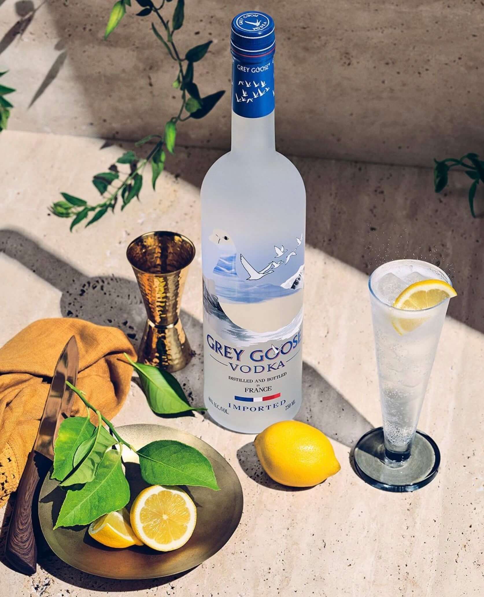 Grey Goose Vodka bottle surrounded by fresh lemons and a refreshing cocktail, showcasing premium ingredients and elegant presentation.