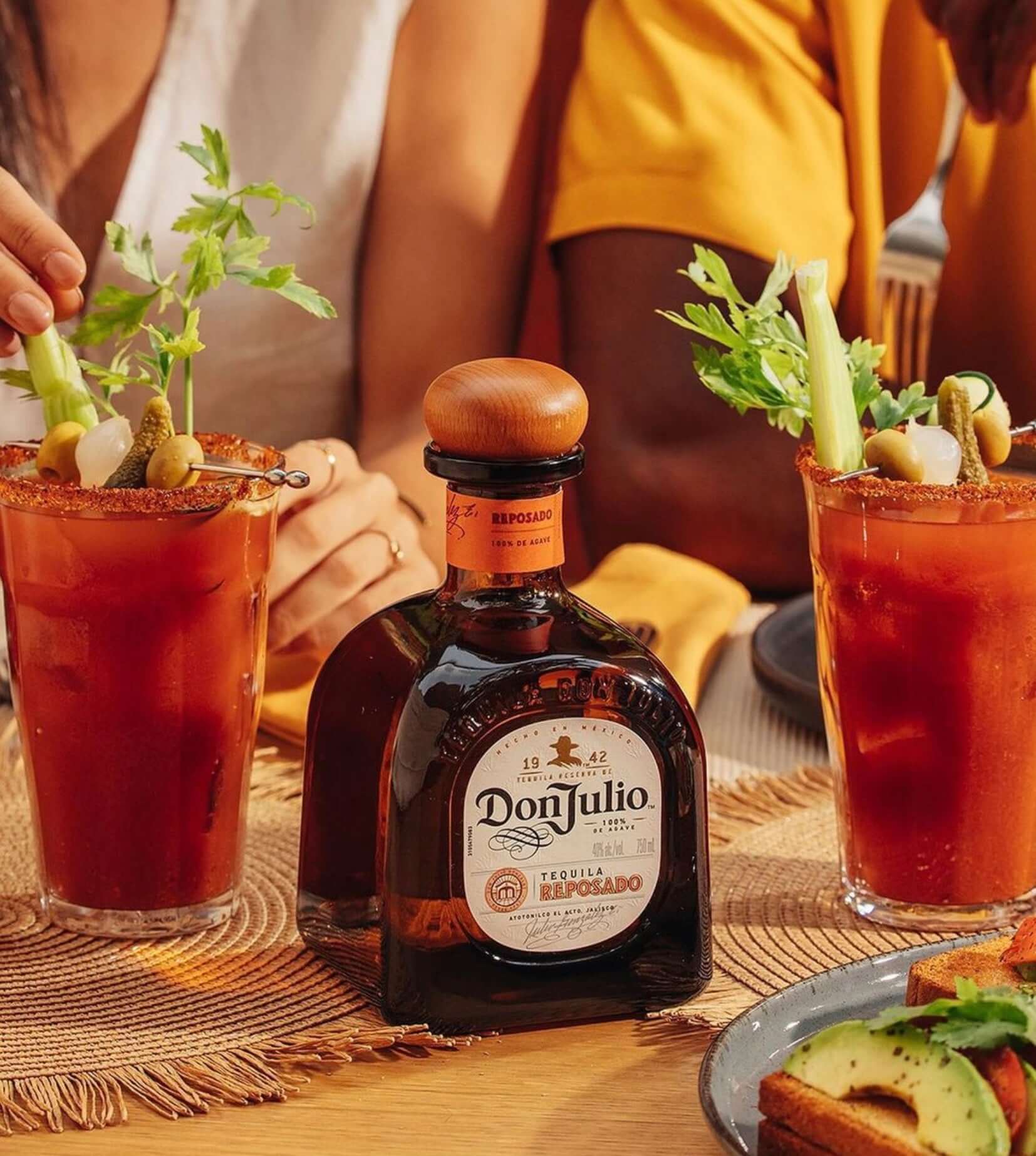 Don Julio Reposado Tequila bottle surrounded by two vibrant cocktails garnished with celery and olives.