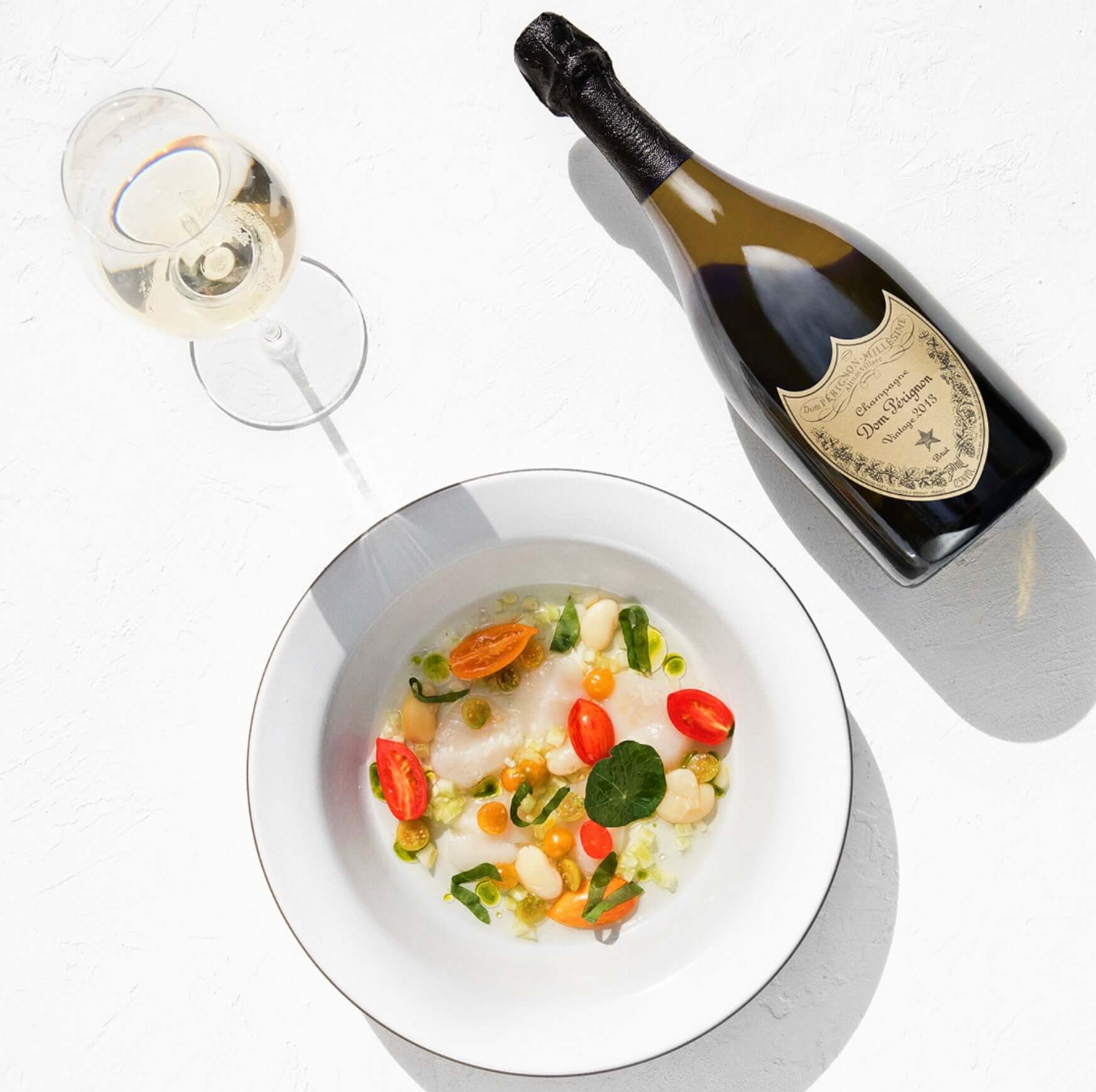 A fine dining setup featuring Dom Pérignon 2013 Brut Champagne and a gourmet vegetable dish.