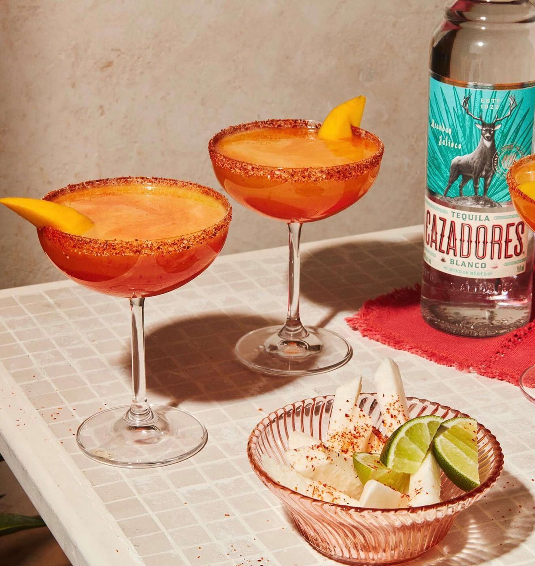 Two margaritas with Cazadores Blanco tequila, garnished with mango and chili, served with fruit and lime.