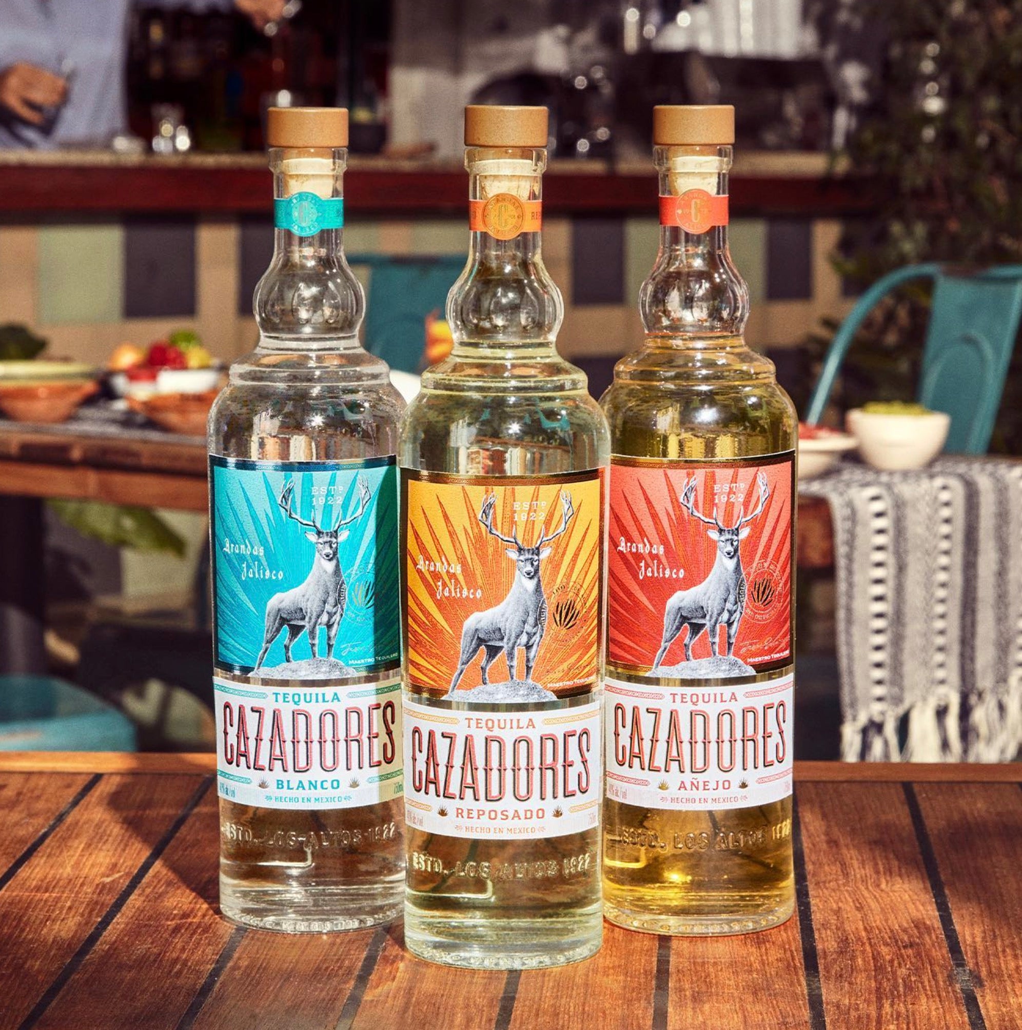 Cazadores Reposado, Añejo, and Blanco tequila bottles displayed on a wooden table, showcasing vibrant labels and unique flavors.