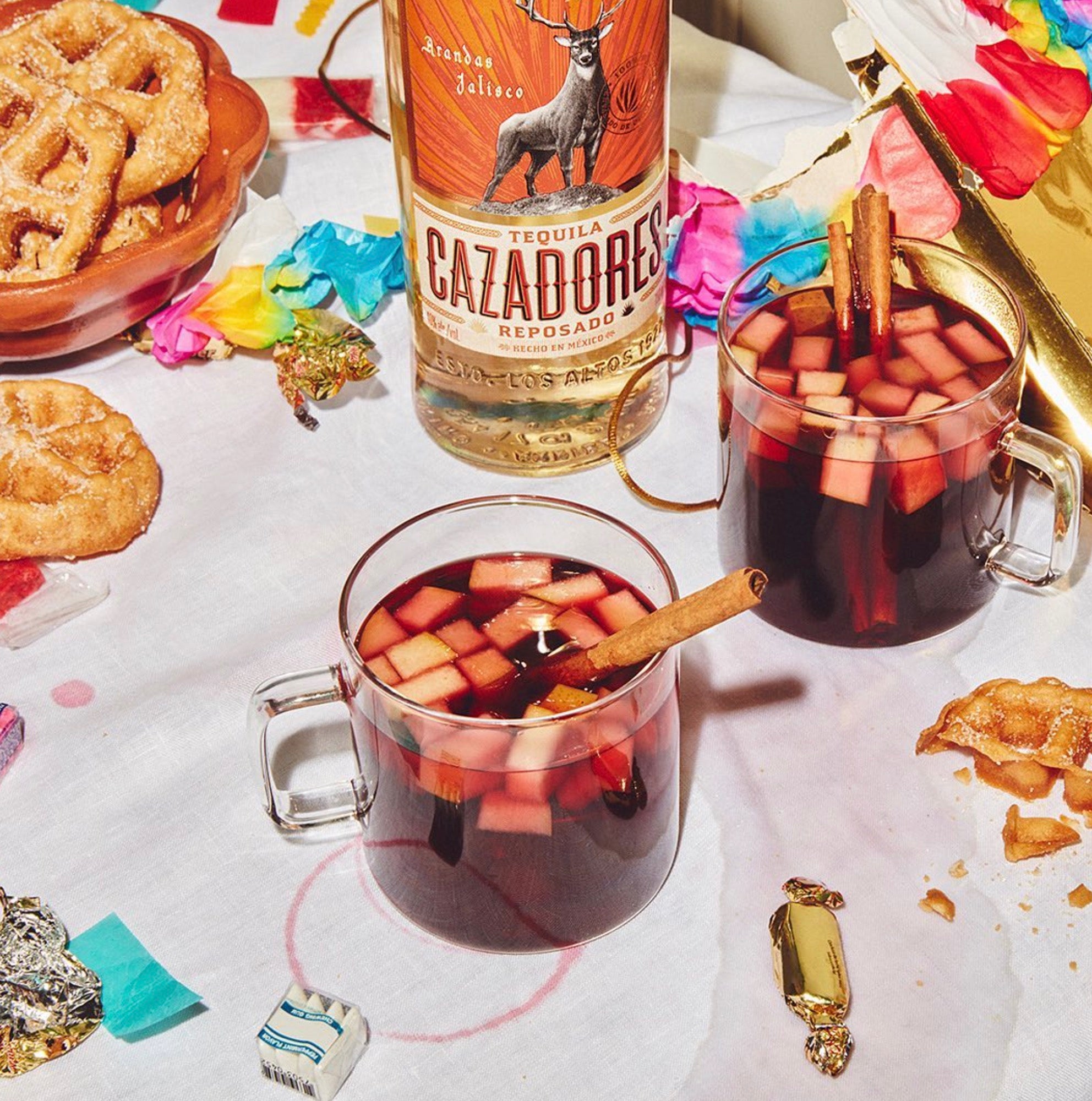 Two glasses of Cazadores Reposado cocktails with apple, cinnamon, and snacks on a decorated table.