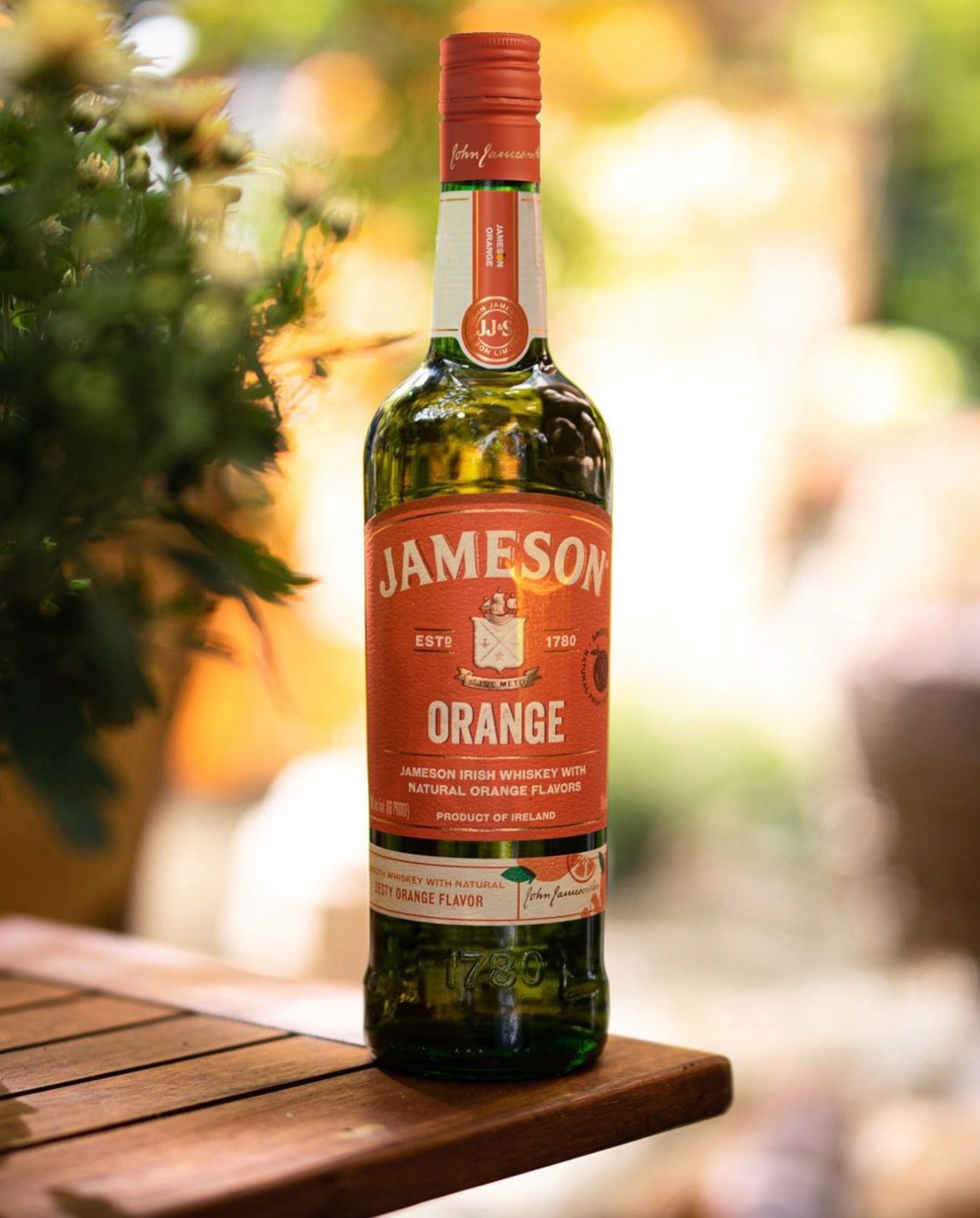 Bottle of Jameson Orange Irish Whiskey featuring natural orange flavors, set against a blurred garden background.