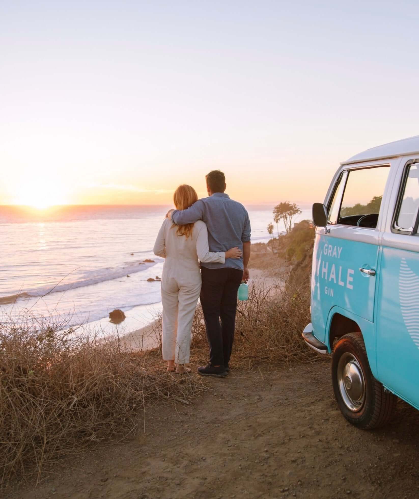 Couple enjoying sunset at the beach beside a Gray Whale Gin branded van, capturing California's essence.