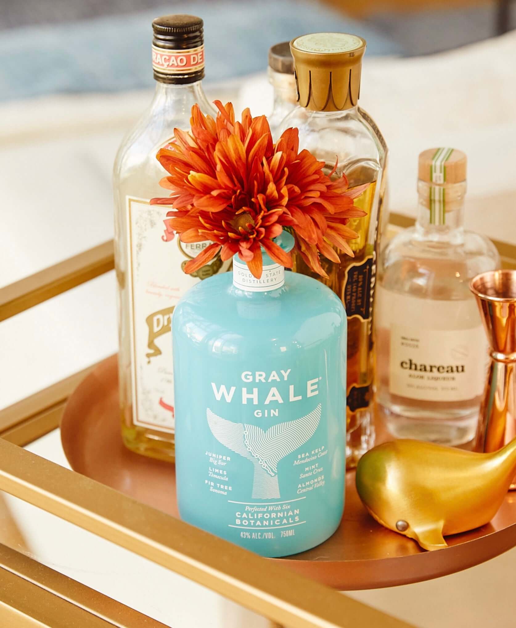Gray Whale Gin bottle with local botanicals and a flower, surrounded by other spirits on a golden tray.