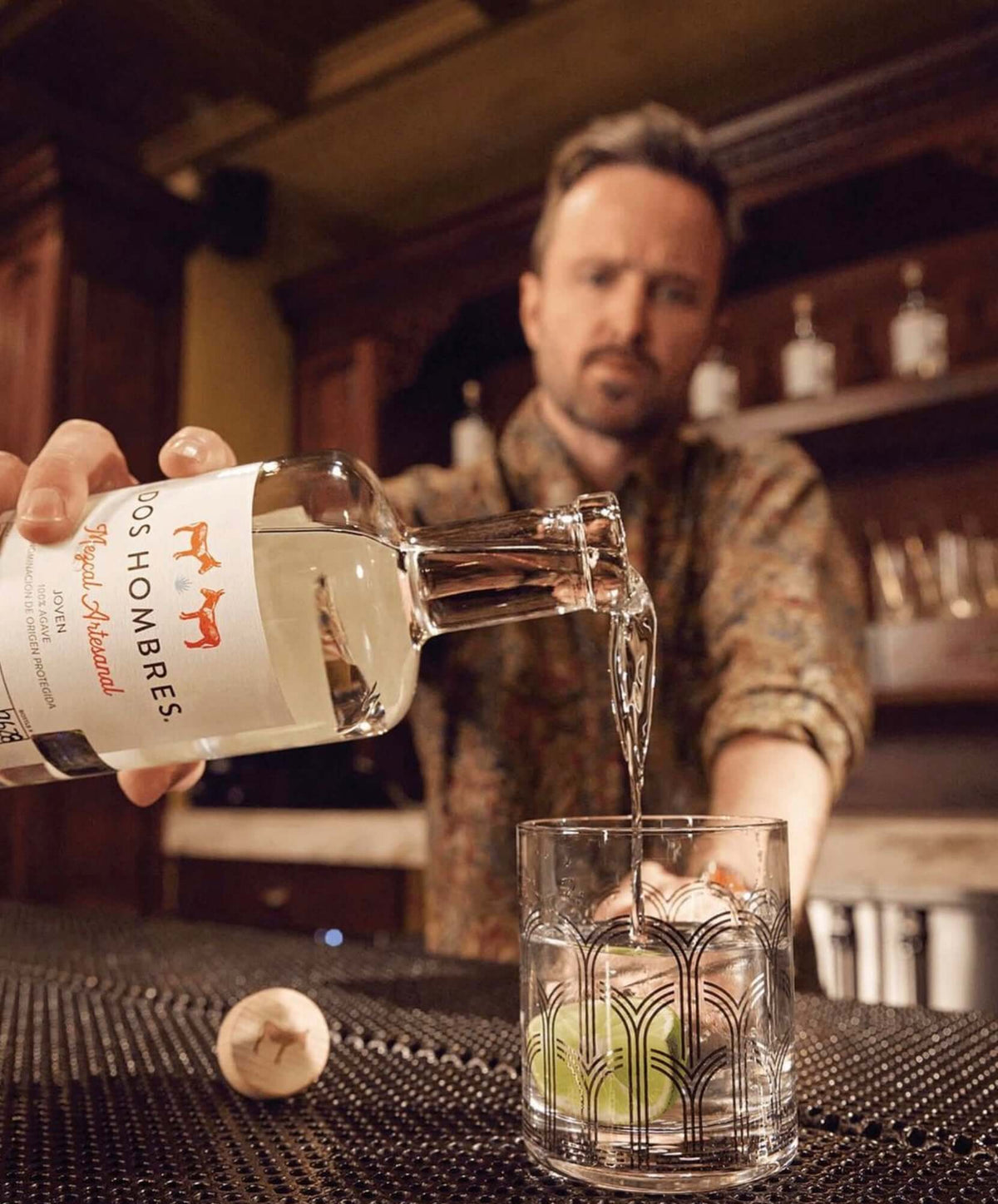 A bartender pouring Dos Hombres Mezcal Espadin Joven into a glass with lime, showcasing its smooth texture and elegance.
