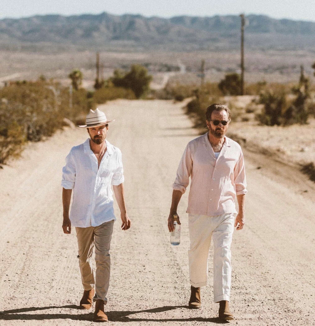 Two men walking down a desert road, showcasing Dos Hombres Mezcal in a natural setting.