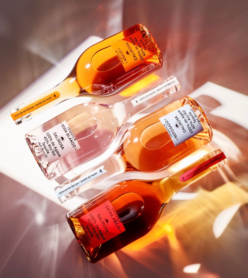 Four bottles of Calirosa Reposado Tequila showcasing their distinctive colors and labels with soft lighting.