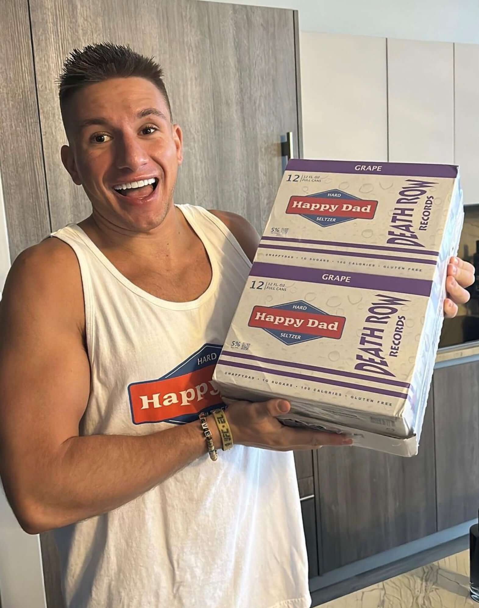 Man holding a 12-pack of Happy Dad X Death Row Records Grape Hard Seltzer, showcasing excitement and enjoyment.