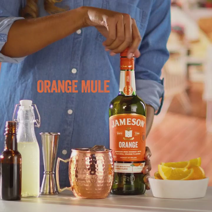 Person preparing an Orange Mule cocktail with Jameson Orange Irish Whiskey, garnished with fresh orange slices.