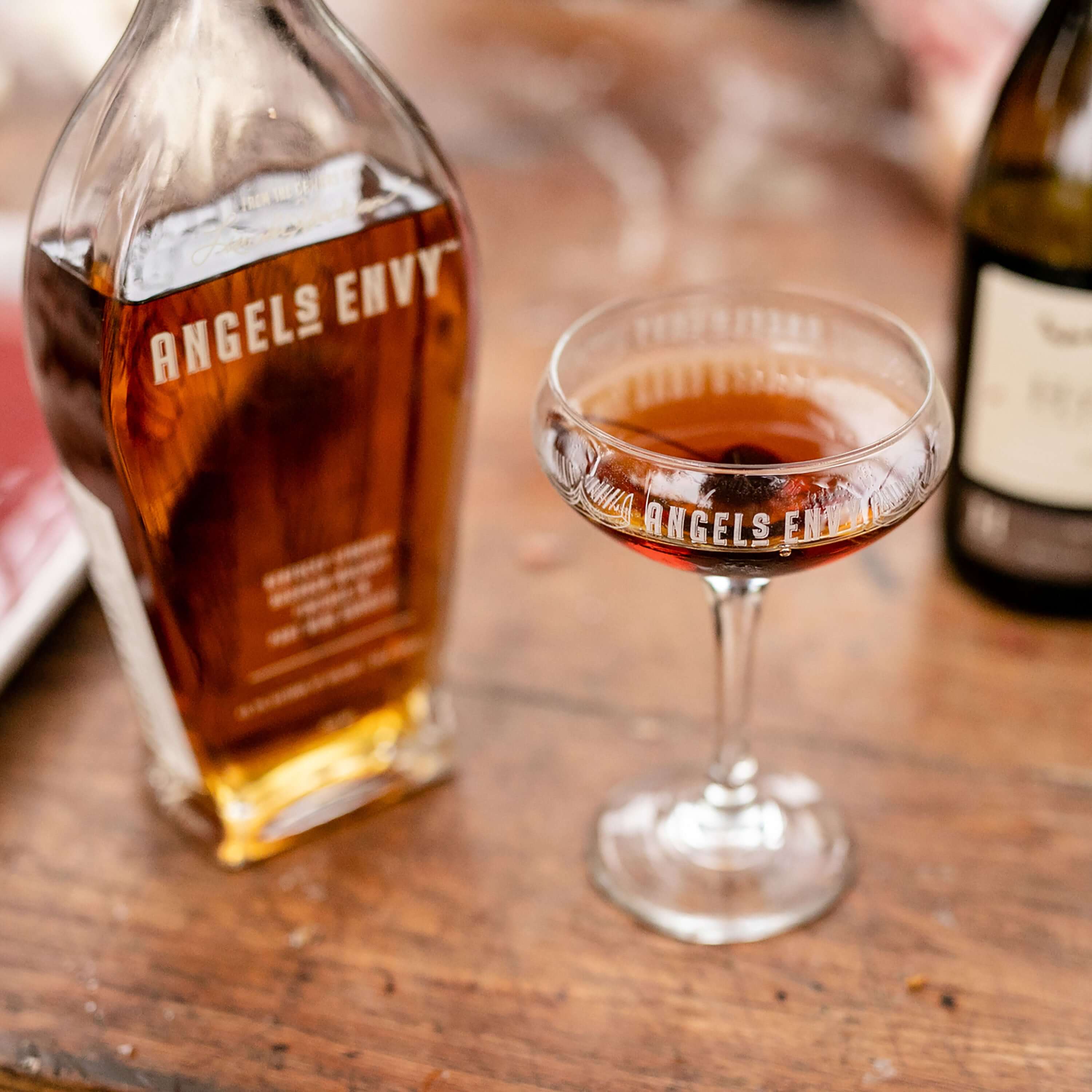 Bottle of Angel's Envy Kentucky Straight Bourbon beside a cocktail glass on a wooden table.