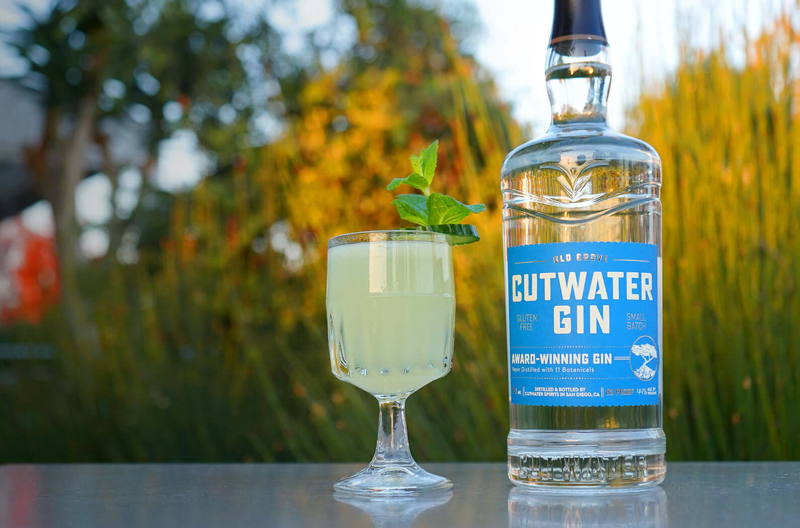 Cutwater Old Grove Gin bottle with a refreshing cocktail, garnished with mint, set against a natural background.