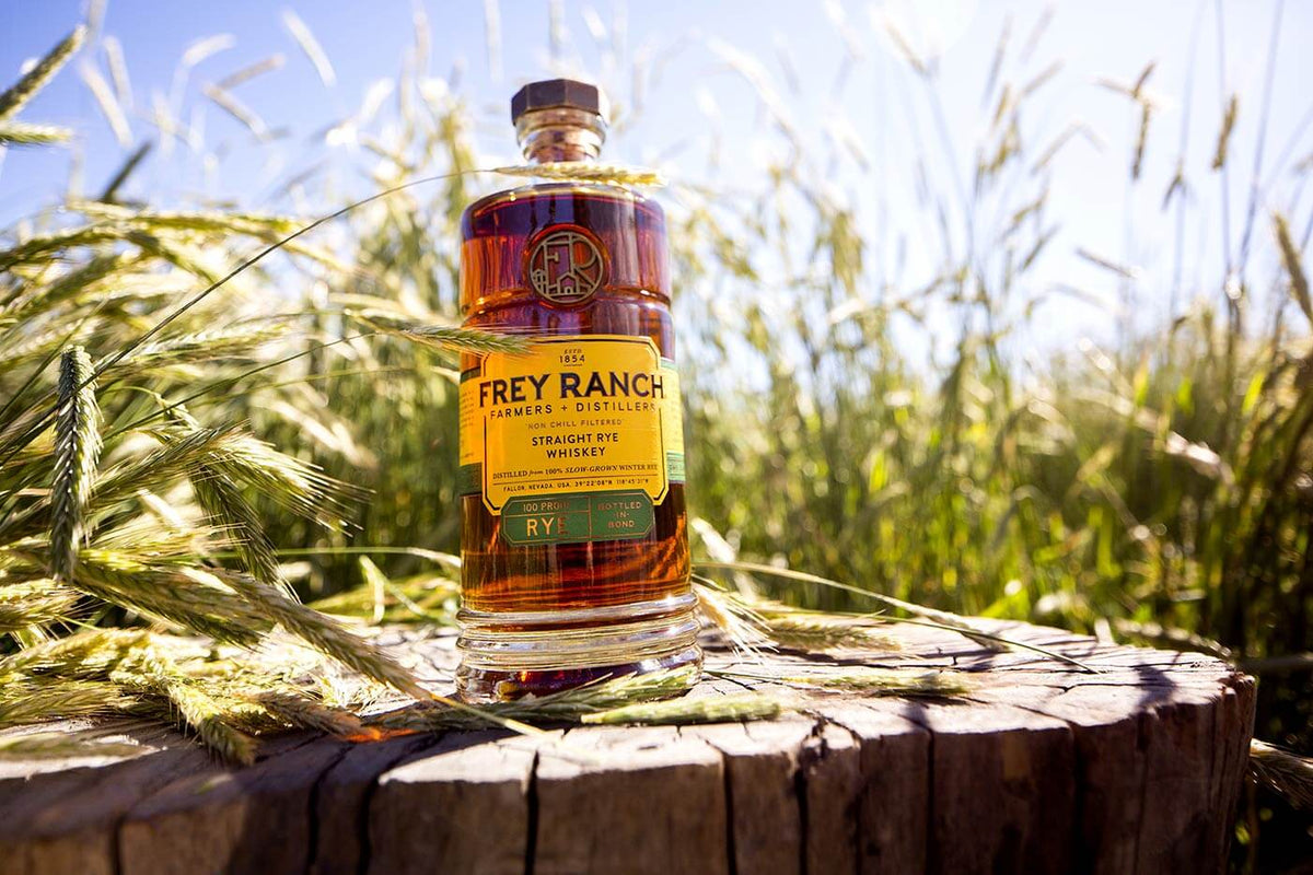 Frey Ranch Bottled-in-Bond Straight Rye Whiskey on a wooden stump surrounded by green wheat fields.