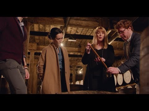 Group of people discussing whiskey production in a distillery, showcasing engagement in the craft of aging spirits.