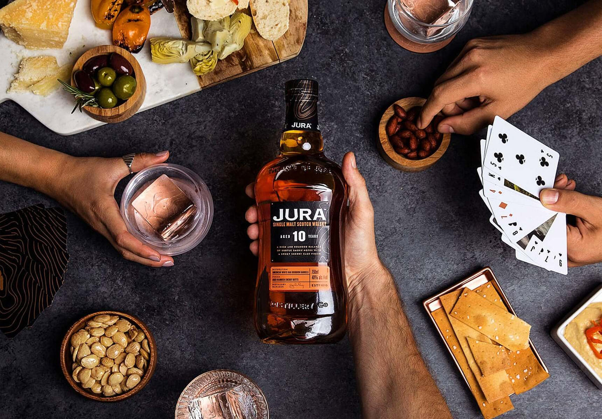 Jura 10 Year Old Scotch Whisky bottle surrounded by snacks and friends enjoying a game night.