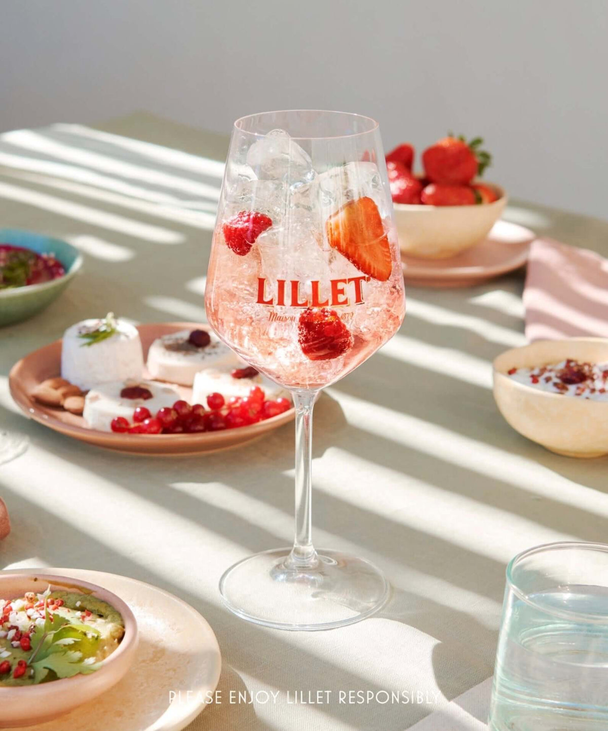 Refreshing Lillet Aperitif Rosé cocktail with strawberries and ice in a stylish glass, served with sweet appetizers.