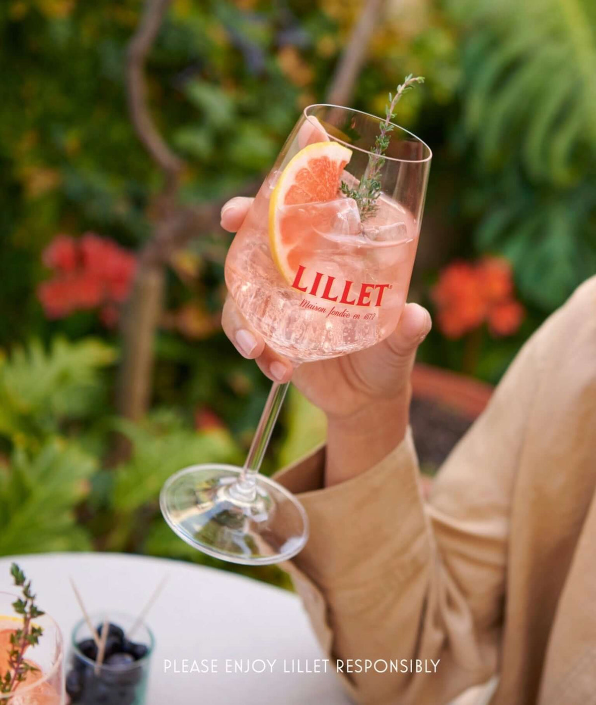 Woman holding a Lillet Rosé aperitif cocktail garnished with grapefruit and thyme in a stylish glass.