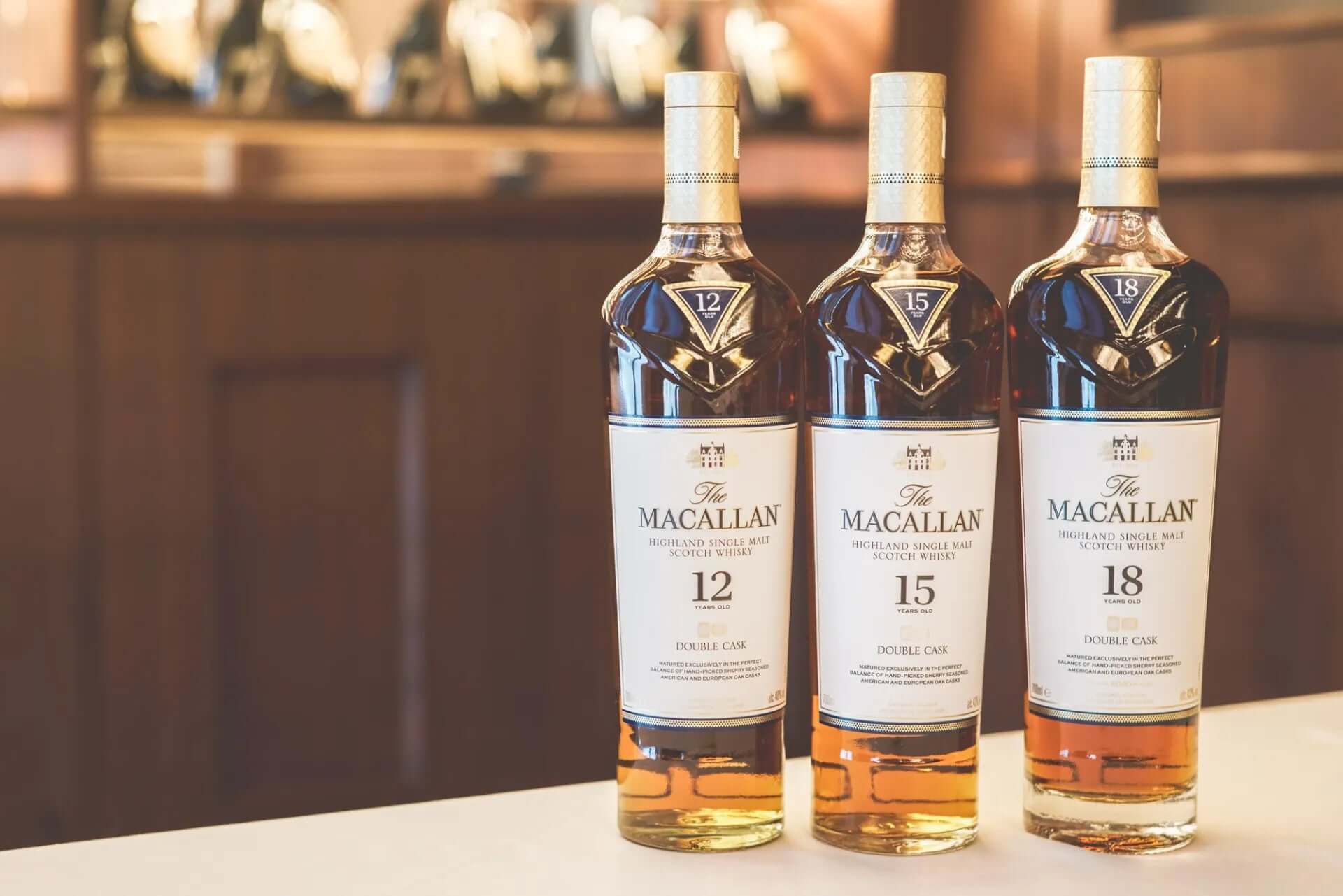 The Macallan Double Cask 15 Year whisky surrounded by 12 and 18 year aged bottles on a bar counter.