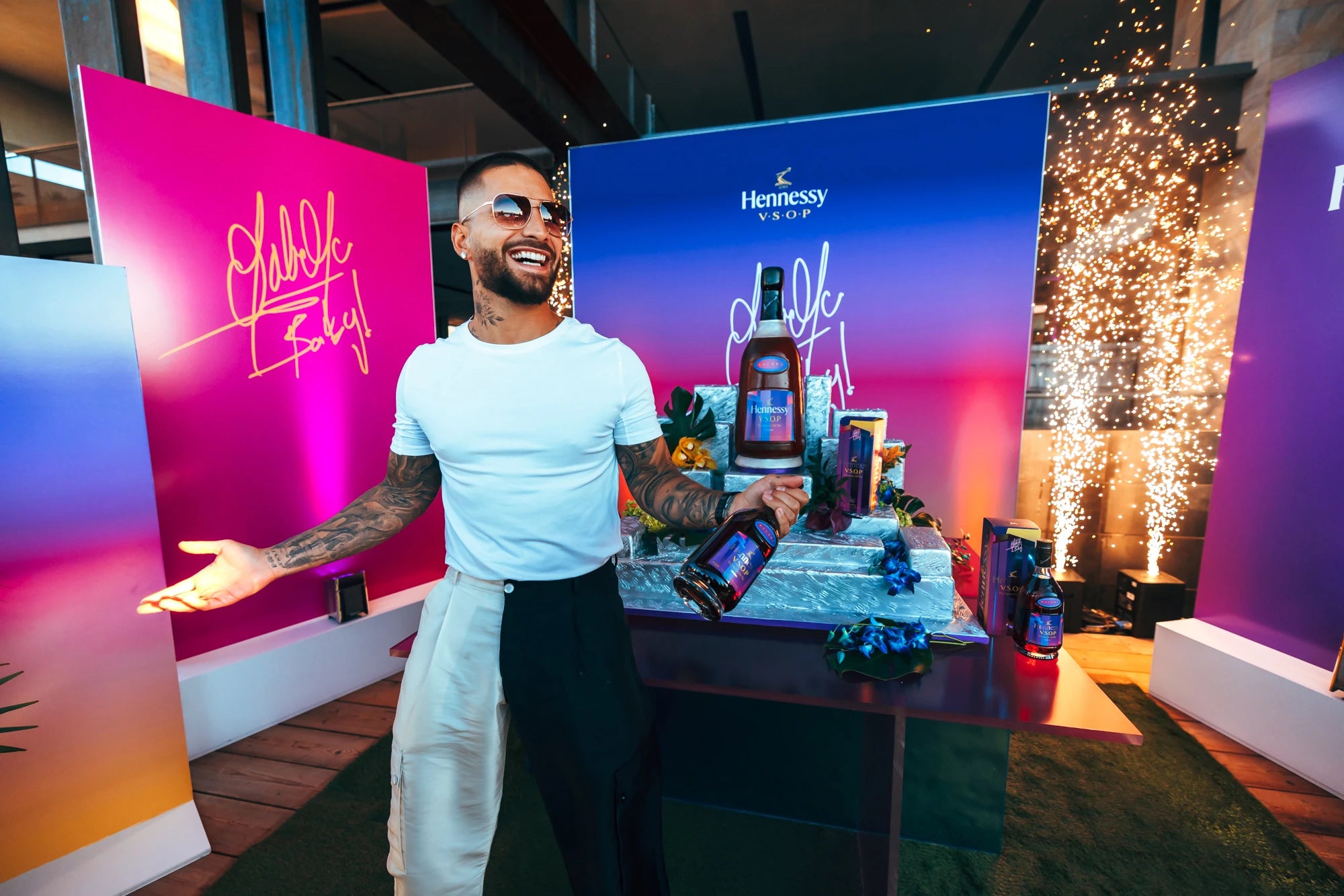 Hennessy V.S.O.P x Maluma event with colorful backdrop, sparkling display, and drinks on the table; celebrating cognac heritage.
