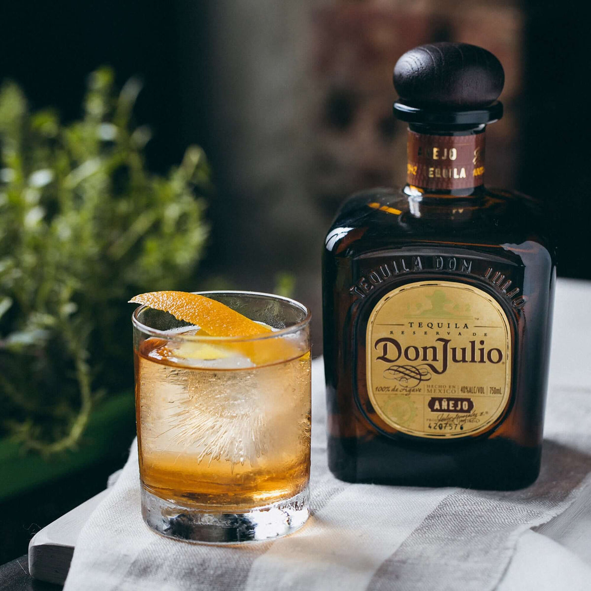 Don Julio Añejo Tequila bottle with a glass of tequila and orange twist on a table.