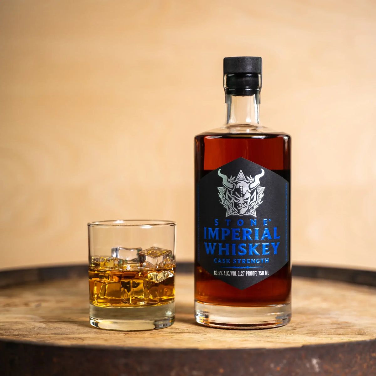 Stone Imperial Whiskey Cask Strength bottle and glass with whiskey on a wooden surface, showcasing rich colors and craftsmanship.
