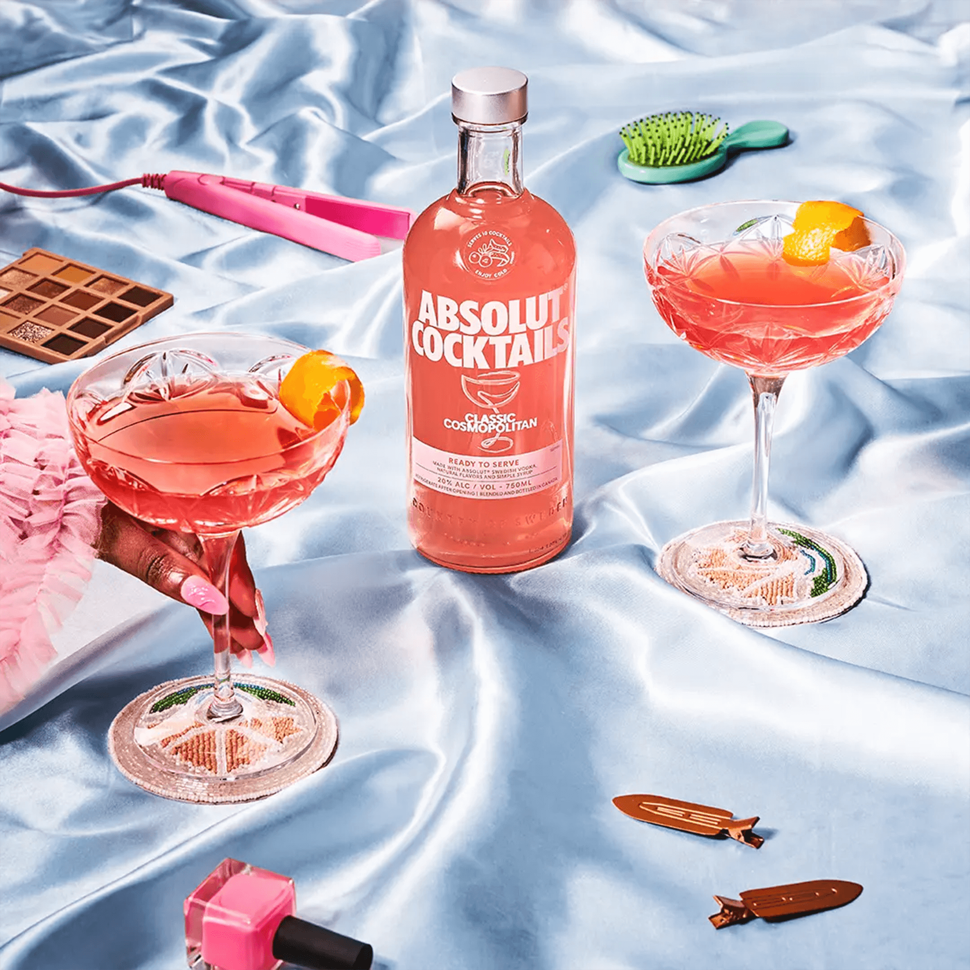 Absolut Cocktails Classic Cosmopolitan bottle with two glasses on a silky surface, garnished and ready to enjoy.