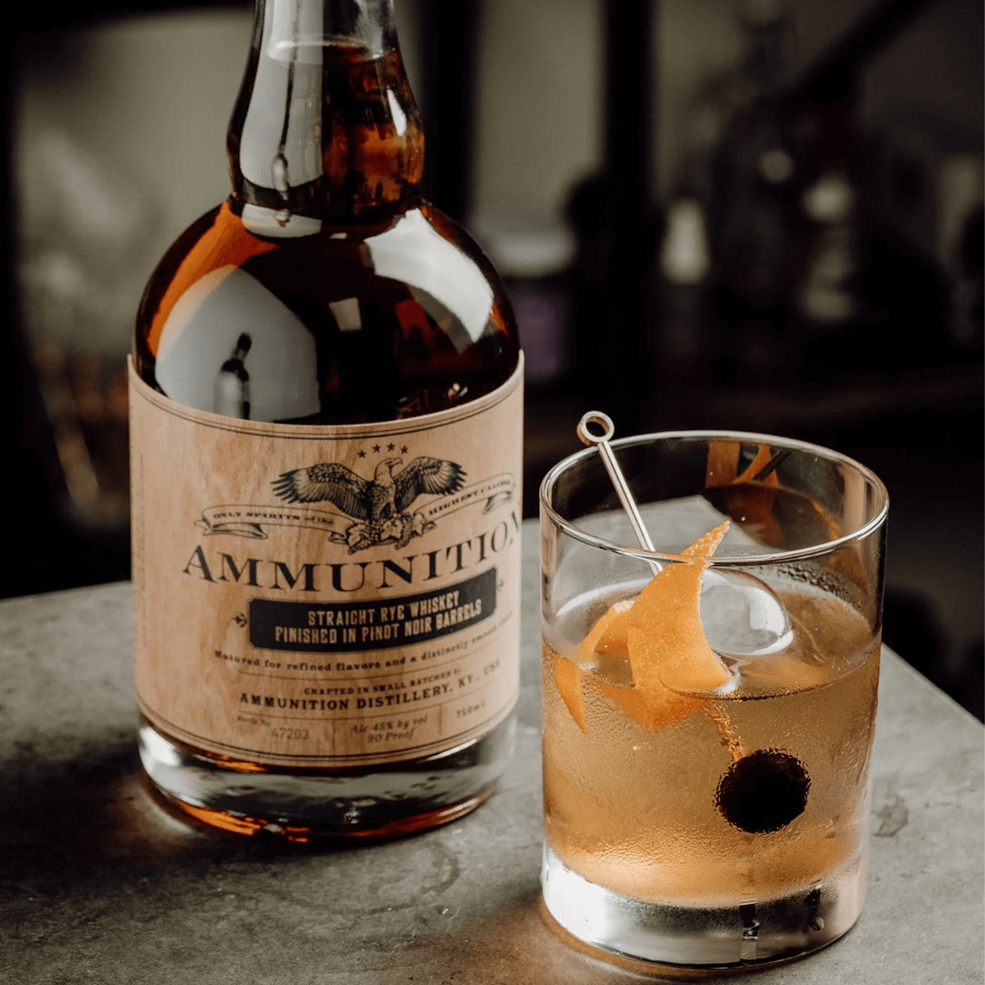 Ammunition Straight Rye Whiskey bottle next to a poured whiskey cocktail with an orange twist.