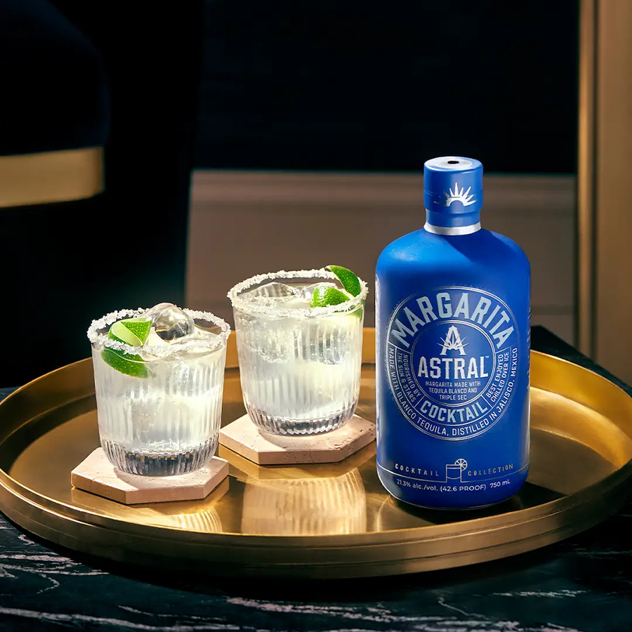 Astral Margarita cocktail with a blue bottle and two glasses on a tray, showcasing citrus flavors and a refreshing drink.