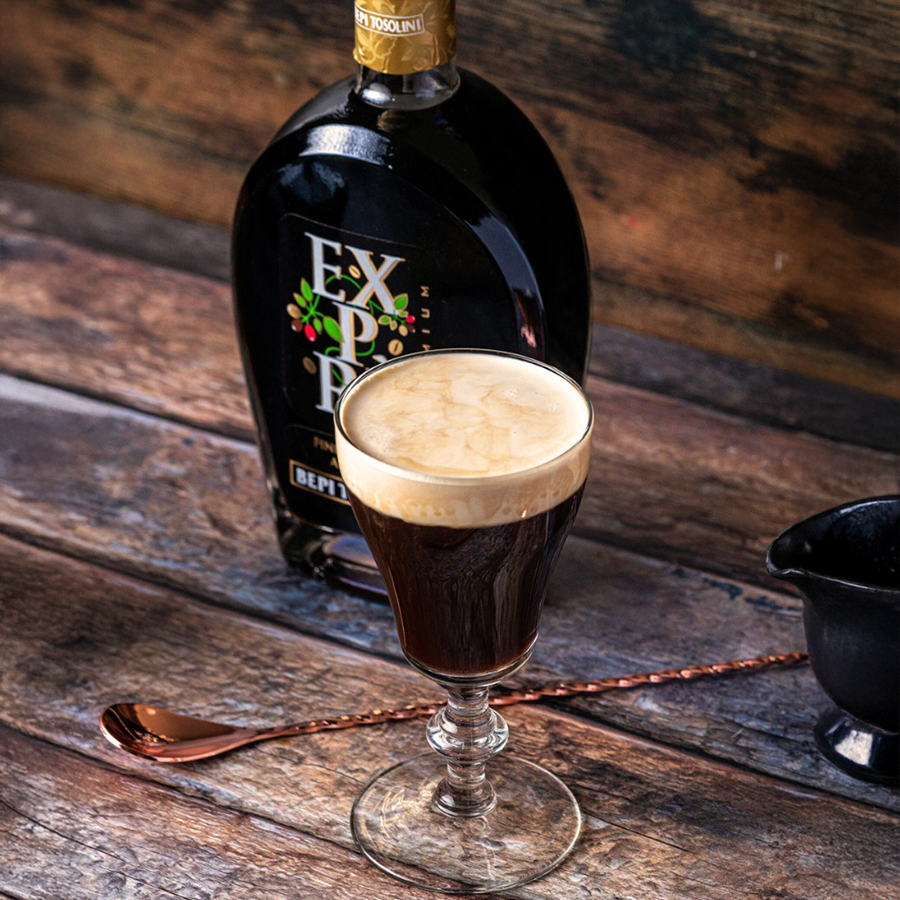 Bepi Tosolini Expre Coffee Liqueur served in a glass with the bottle in the background, showcasing rich coffee color and foam.