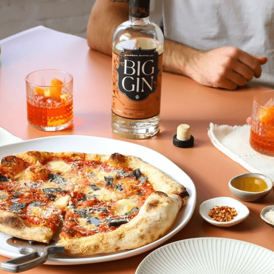 A table setting with pizza, Big Gin bourbon barrel gin, and cocktails, perfect for a cozy dining experience.