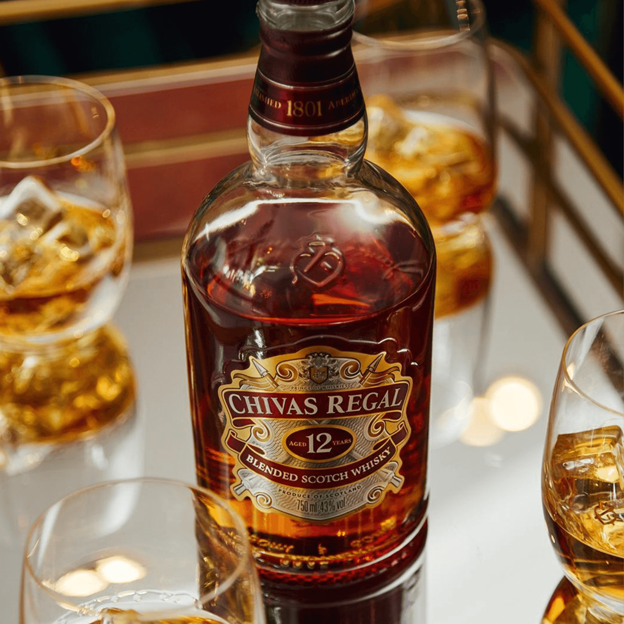 Chivas Regal 12 Year Blended Scotch Whiskey bottle surrounded by glasses of whiskey with ice.