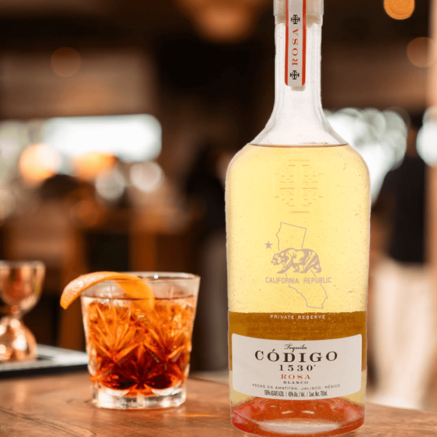 Código 1530 Rosa Tequila bottle with a cocktail and an orange garnish on a bar counter.