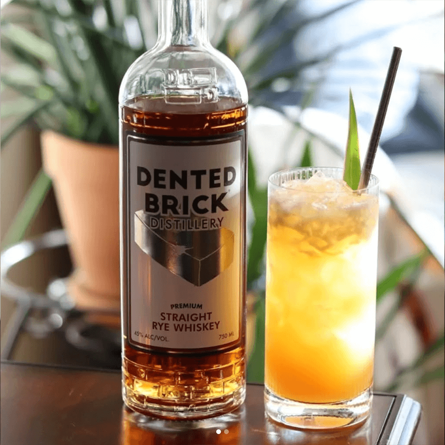Dented Brick Premium Straight Rye Whiskey bottle beside a refreshing cocktail, showcasing premium craftsmanship and flavor.