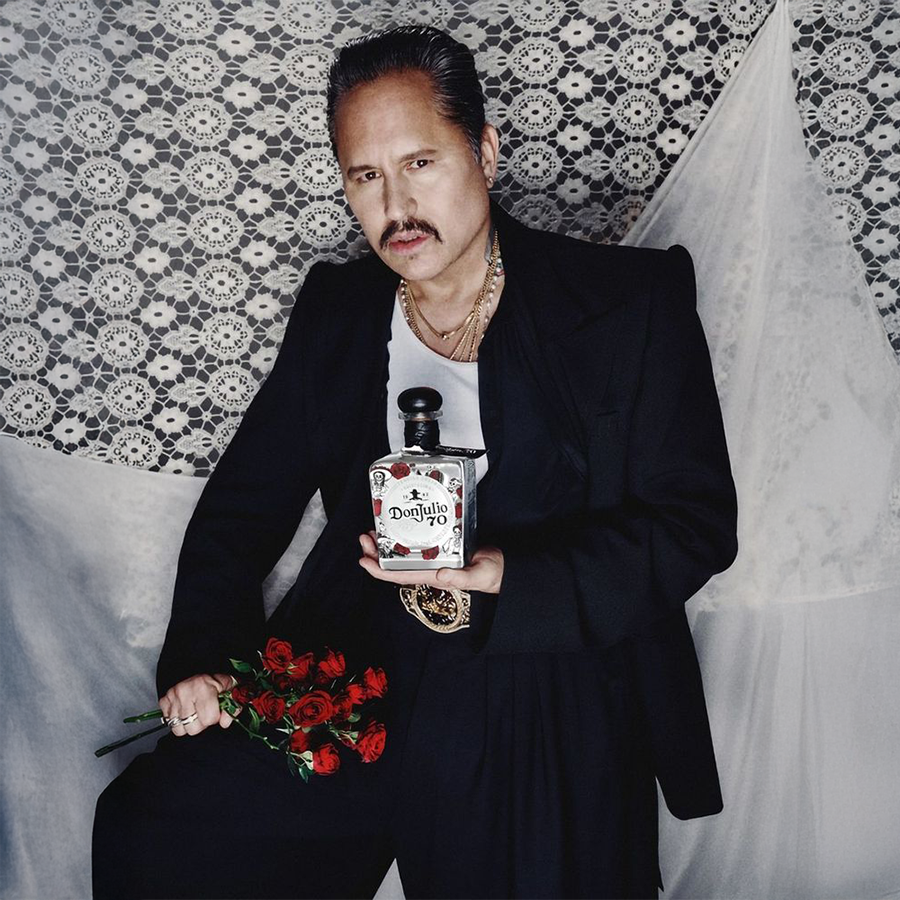 Don Julio 70 Dia De Los Muertos bottle held by a stylish man with roses, celebrating Día de los Muertos.
