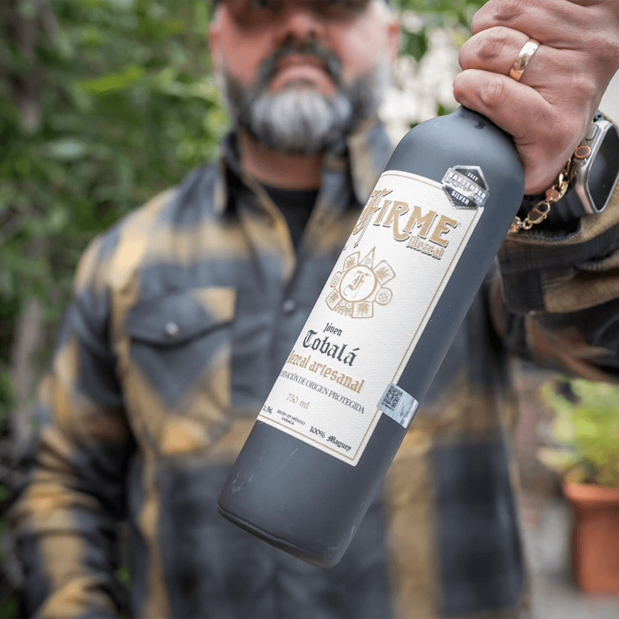 Firme Mezcal Joven Tobala held by a person, showcasing the unique bottle design and artisanal quality.