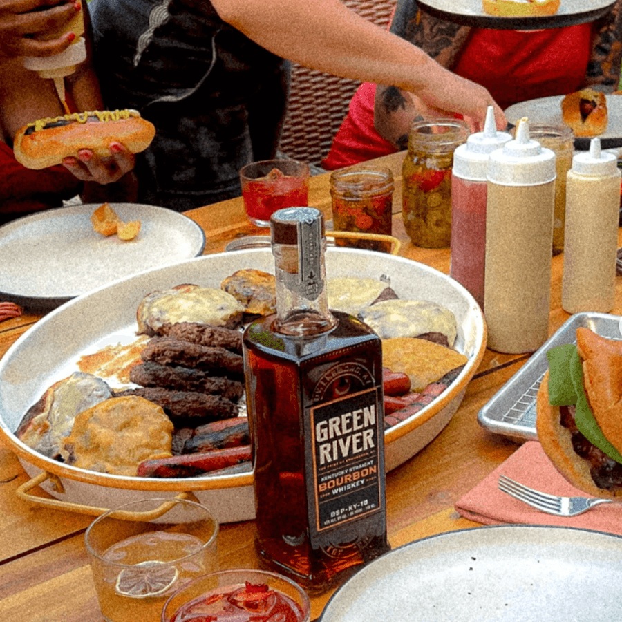 Green River Full Proof Bourbon showcased at a summer barbecue alongside burgers and hot dogs.