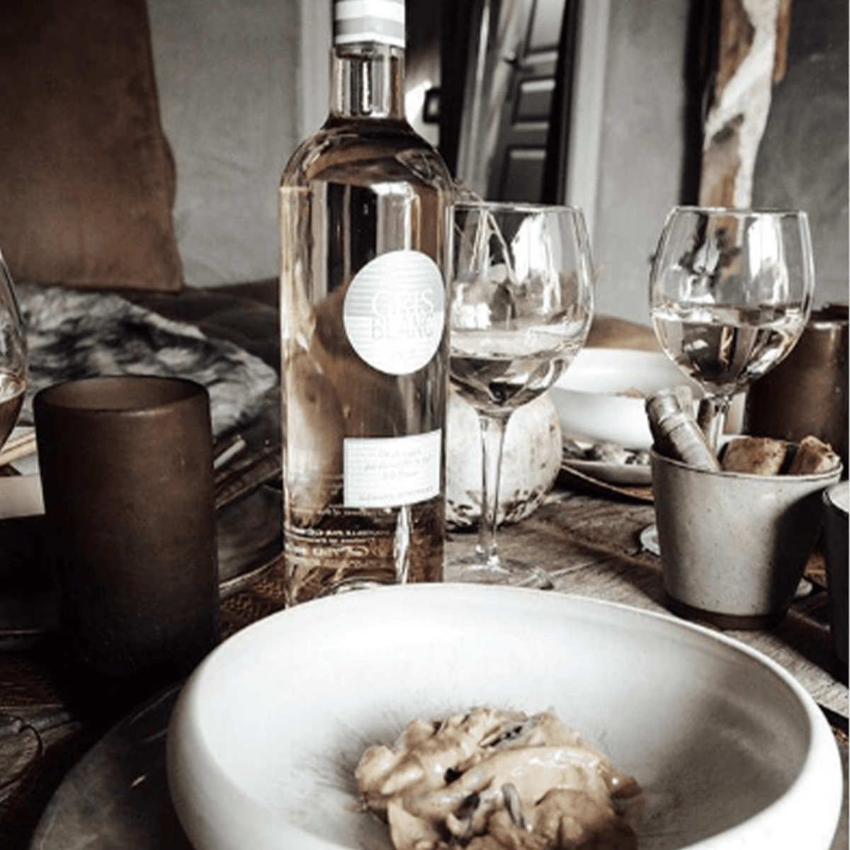 Bottle of Gris Blanc Rosé on a dining table with glasses and a plate of food, showcasing a chic dining setting.