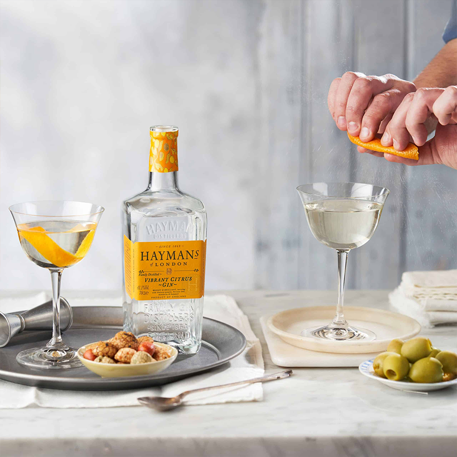 Hayman's Vibrant Citrus Gin bottle with cocktails and garnishes on a table, showcasing Citrus Gin's vibrant flavors.