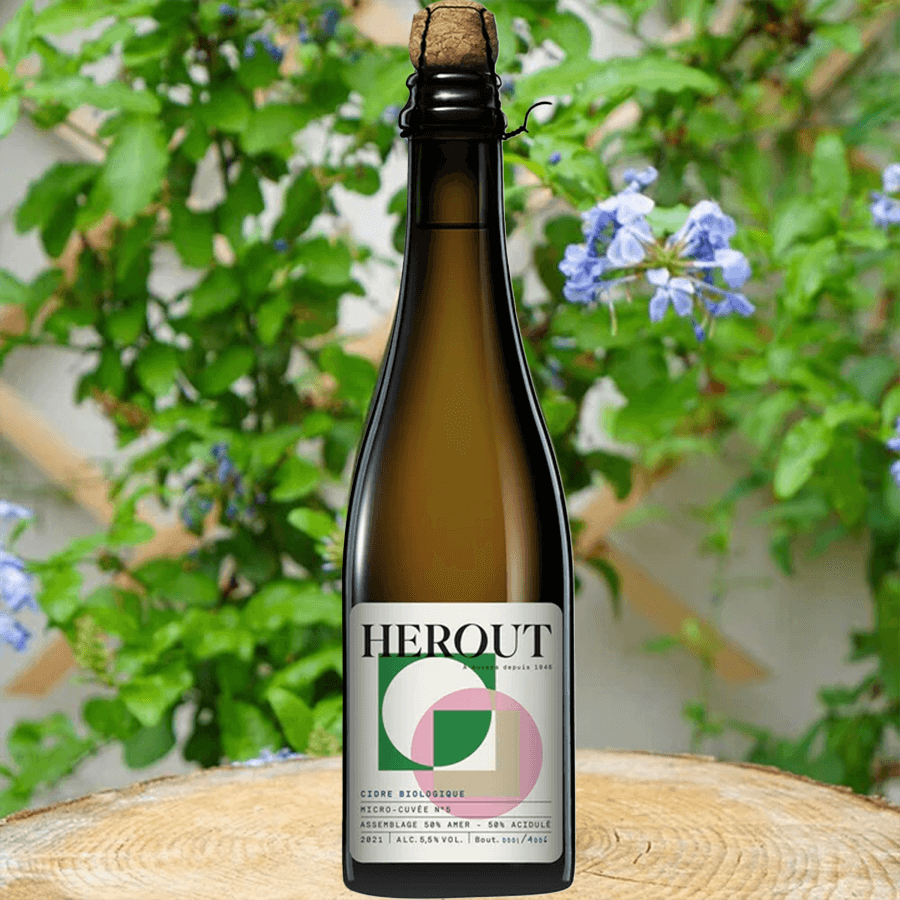 Herout Micro Cuvée No. 5 cider bottle against a floral backdrop, showcasing its sparkling golden color.