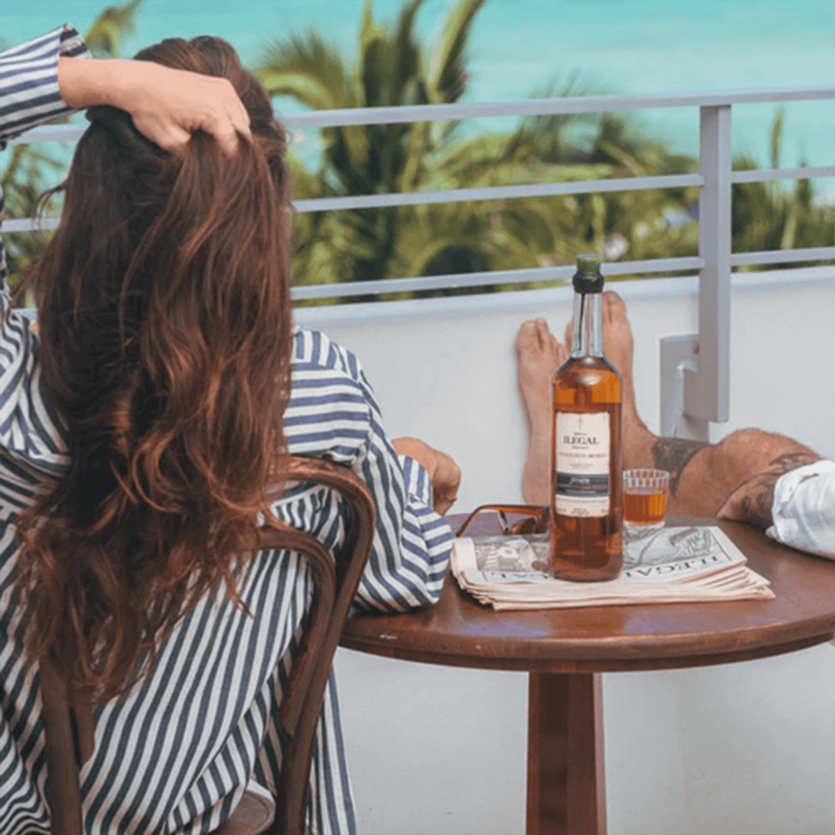Relaxing scene with Ilegal Reposado Caribbean Cask Finish Mezcal on table amidst tropical backdrop.