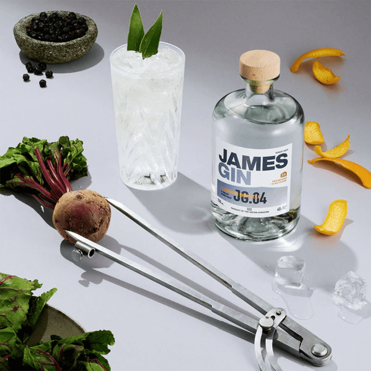 James Gin London Drizzle bottle beside a refreshing gin cocktail with fresh ingredients and garnishes.