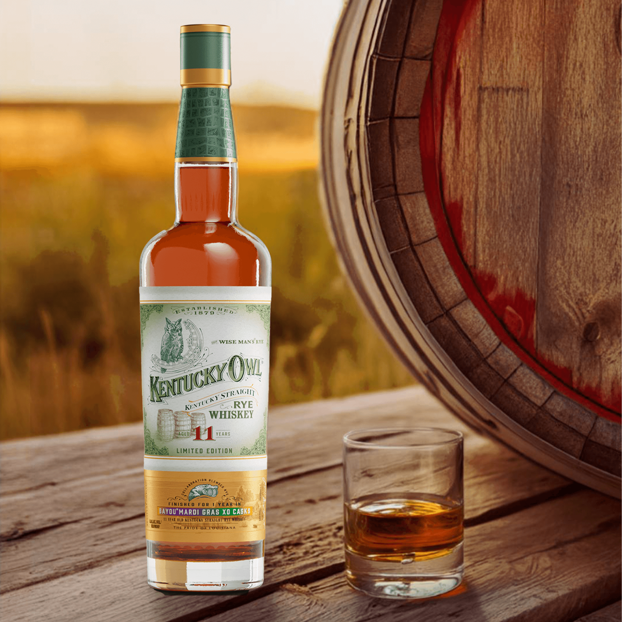 Kentucky Owl Mardi Gras XO Casks Limited Edition Rye Whiskey bottle next to a glass on a wooden table.
