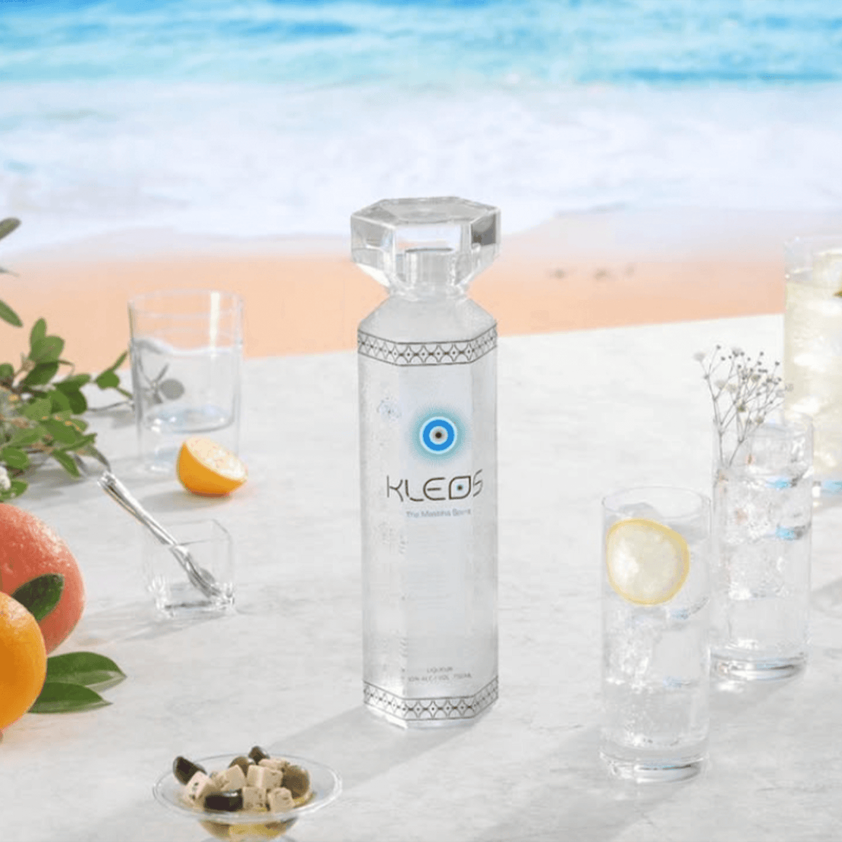 KLEOS Mastiha Spirit bottle with refreshing cocktails by the beach, showcasing its elegant design and vibrant ingredients.