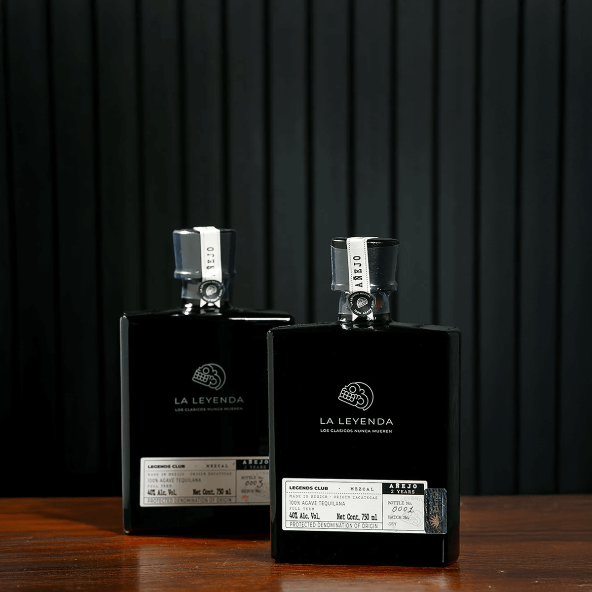 Two bottles of La Leyenda Mezcal Añejo displayed on a wooden surface, showcasing elegant packaging and labels.