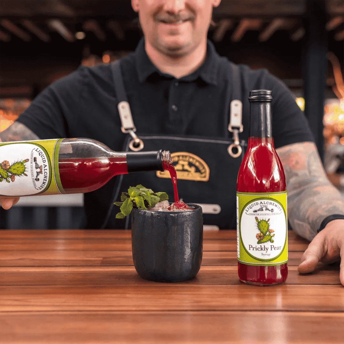 Bartender pouring Liquid Alchemist Prickly Pear Syrup into a drink, showcasing vibrant cocktail preparation.